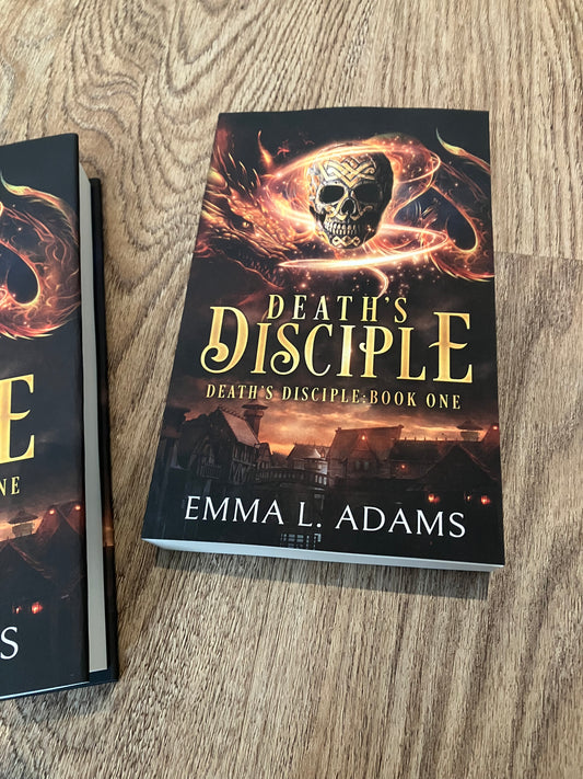 A paperback of Death's Disciple lying on a wood grain floor